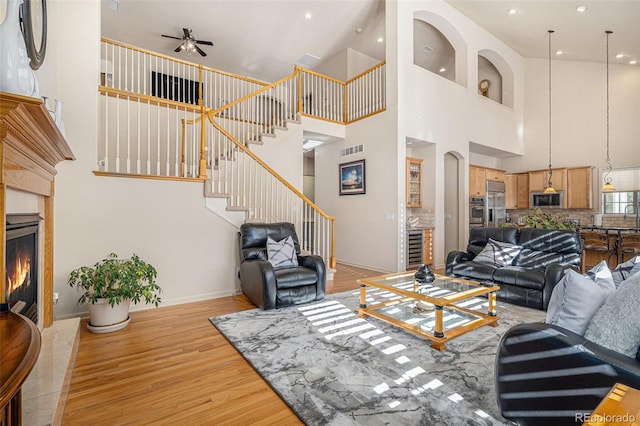 living room with light wood-type flooring, ceiling fan, beverage cooler, a high ceiling, and a tiled fireplace