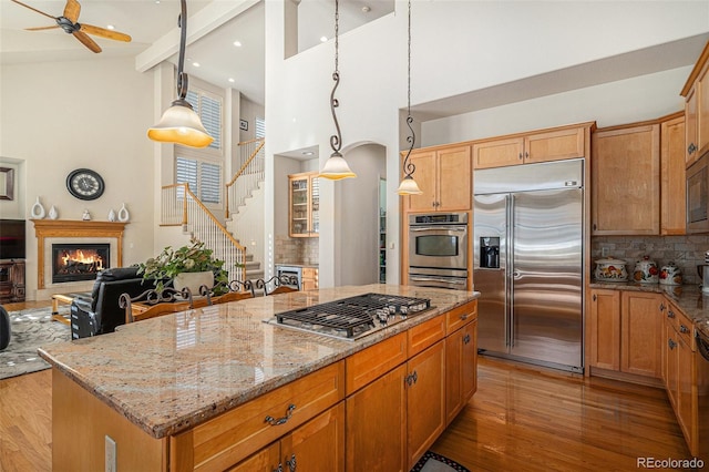 kitchen with beam ceiling, light stone counters, built in appliances, decorative backsplash, and a kitchen island