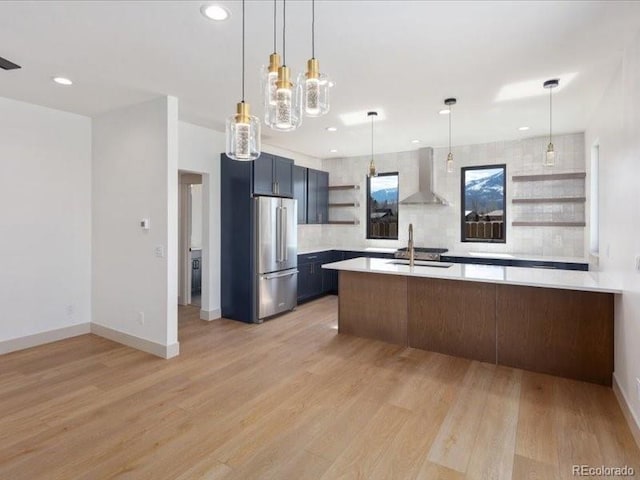 kitchen with light countertops, wall chimney range hood, freestanding refrigerator, open shelves, and light wood finished floors