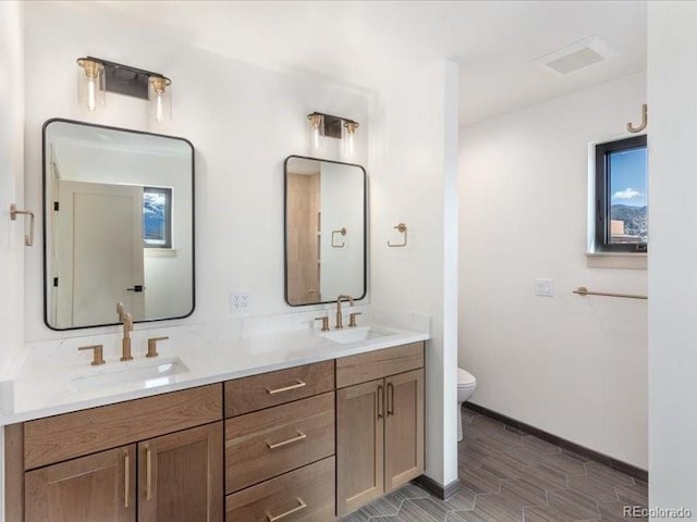 full bath featuring baseboards, a sink, toilet, and double vanity