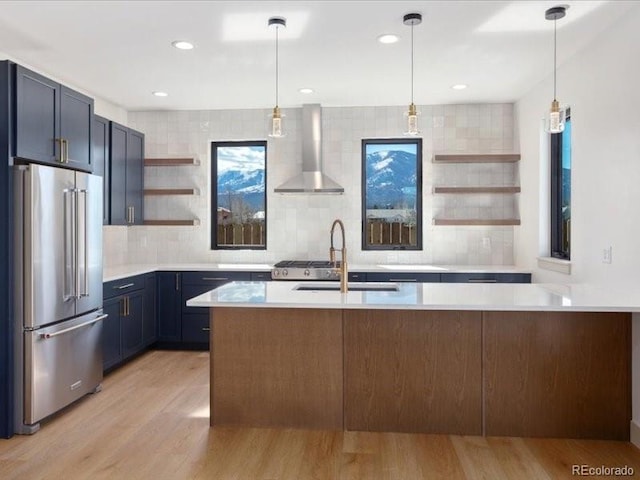 kitchen with high end fridge, light countertops, wall chimney range hood, open shelves, and a sink