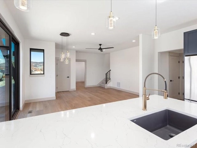 kitchen with pendant lighting, a sink, freestanding refrigerator, and light stone countertops