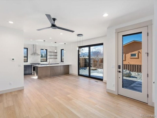 interior space featuring wall chimney exhaust hood, light countertops, light wood-type flooring, stainless steel range oven, and pendant lighting