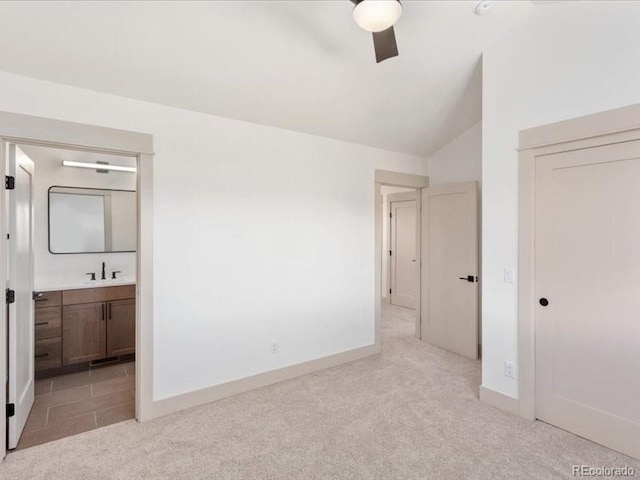 unfurnished bedroom featuring light carpet, ensuite bath, a sink, vaulted ceiling, and a closet