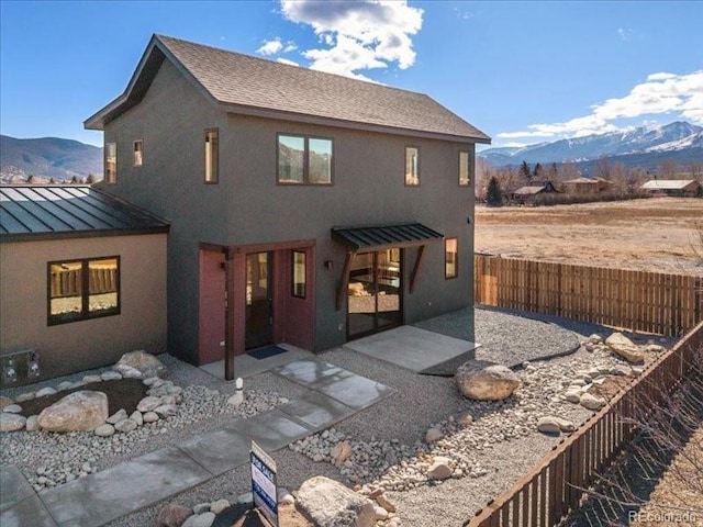 rear view of house with a standing seam roof, a mountain view, metal roof, and stucco siding