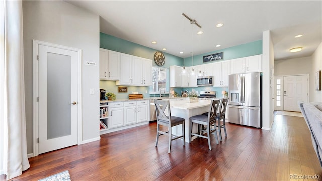 kitchen featuring appliances with stainless steel finishes, white cabinetry, a breakfast bar, decorative light fixtures, and a center island