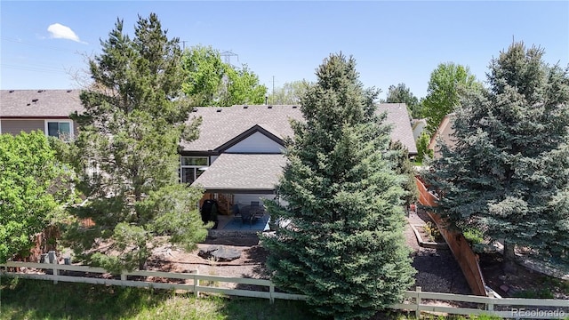 back of property with fence, a patio area, and a shingled roof
