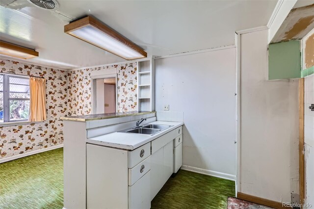 kitchen featuring a peninsula, light countertops, a sink, wallpapered walls, and baseboards