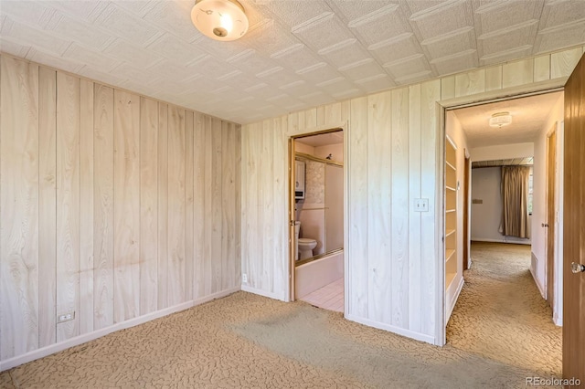 unfurnished bedroom featuring wood walls, baseboards, carpet flooring, and ensuite bathroom