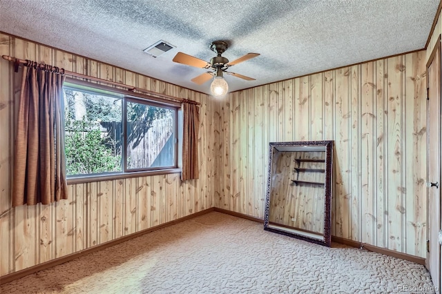 spare room with ceiling fan, baseboards, wooden walls, and visible vents