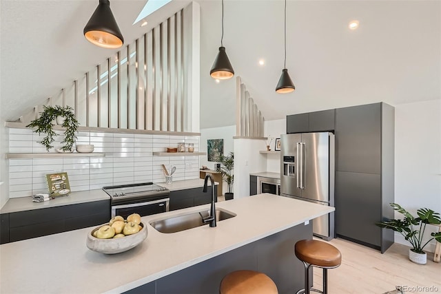 kitchen featuring appliances with stainless steel finishes, a breakfast bar, sink, decorative light fixtures, and light hardwood / wood-style flooring