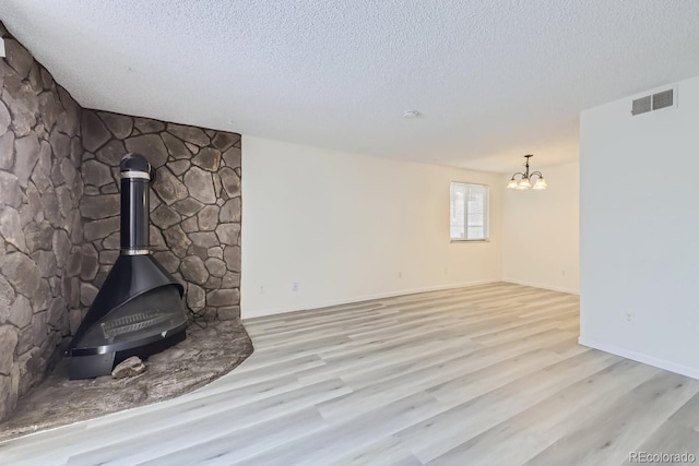 unfurnished living room with a textured ceiling, a notable chandelier, light hardwood / wood-style flooring, and a wood stove