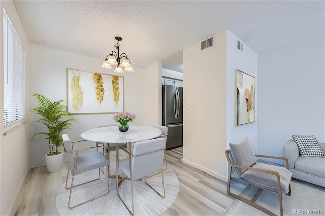 dining space featuring a textured ceiling, light wood-type flooring, and a notable chandelier