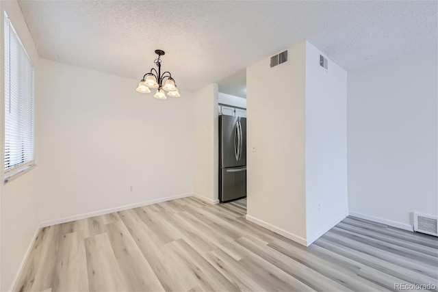 spare room with a textured ceiling, light wood-type flooring, and an inviting chandelier