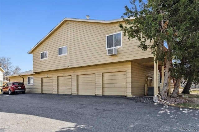 view of side of home featuring an attached garage, a wall mounted AC, stairs, and driveway