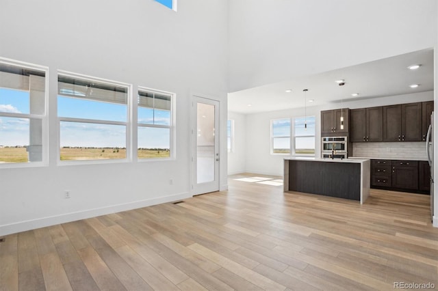 995 Pinehurst Ct, Bennett, CO 80102 - kitchen with open floor plan, dark brown cabinetry, light wood-type flooring, a center island with sink, and light countertops
