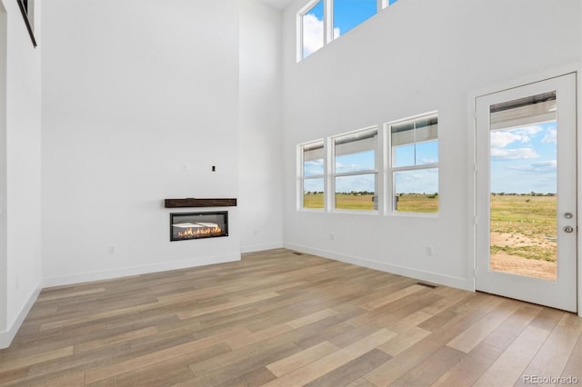 995 Pinehurst Ct, Bennett, CO 80102 - unfurnished living room featuring a towering ceiling, light wood finished floors, and a glass covered fireplace