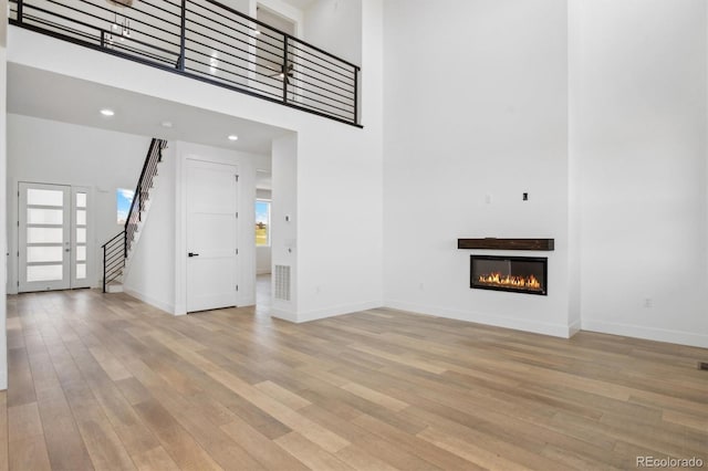 995 Pinehurst Ct, Bennett, CO 80102 - unfurnished living room with stairway, light wood-style floors, a glass covered fireplace, and a high ceiling