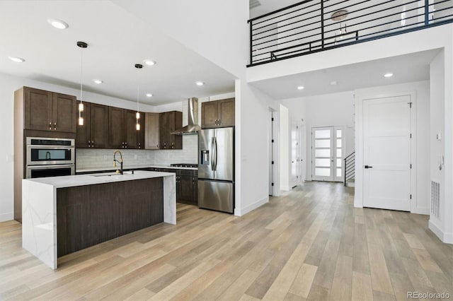 995 Pinehurst Ct, Bennett, CO 80102 - kitchen with stainless steel appliances, wall chimney exhaust hood, dark brown cabinetry, light wood finished floors, and tasteful backsplash