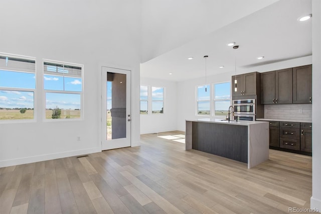 995 Pinehurst Ct, Bennett, CO 80102 - kitchen featuring dark brown cabinetry, stainless steel double oven, light wood finished floors, light countertops, and backsplash