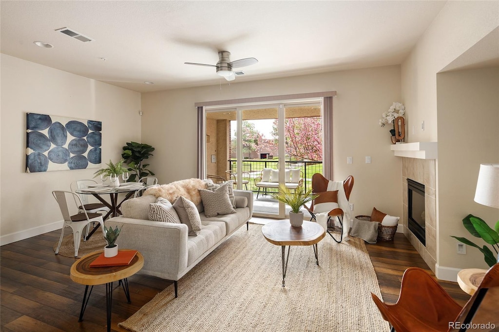 living room featuring baseboards, a tiled fireplace, a ceiling fan, visible vents, and wood finished floors