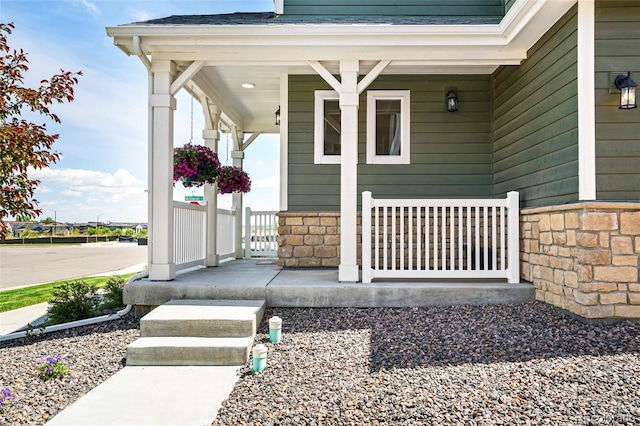 property entrance featuring stone siding, covered porch, and roof with shingles