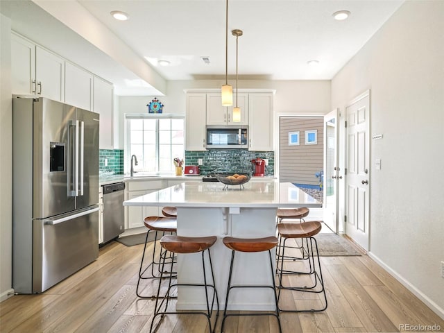 kitchen with a kitchen island, stainless steel appliances, decorative light fixtures, white cabinets, and light hardwood / wood-style floors