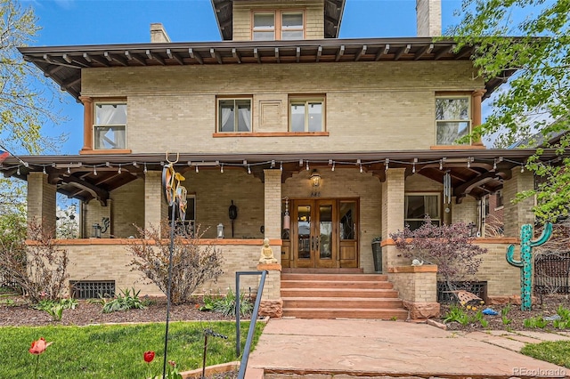 italianate home with covered porch, brick siding, and french doors