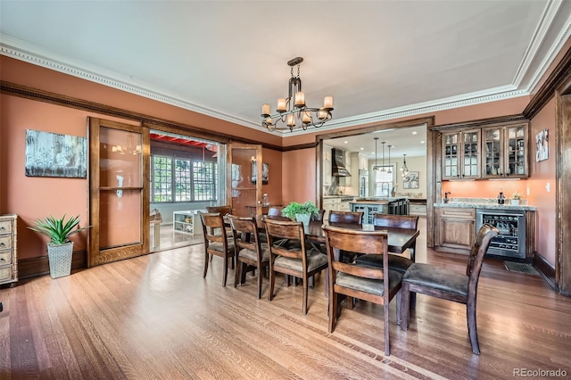dining space featuring wine cooler, crown molding, indoor wet bar, and a notable chandelier