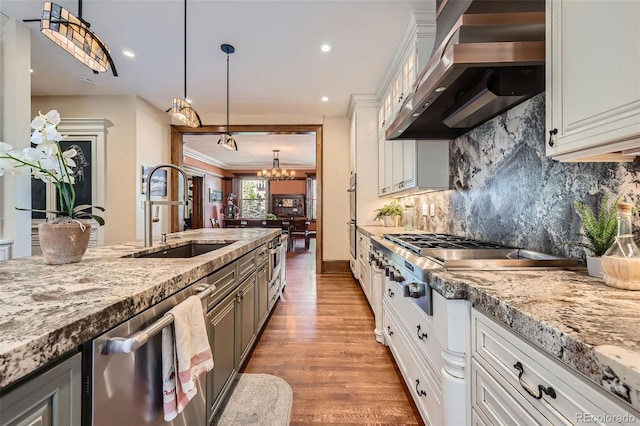 kitchen featuring a notable chandelier, a sink, wall chimney exhaust hood, stainless steel appliances, and decorative backsplash