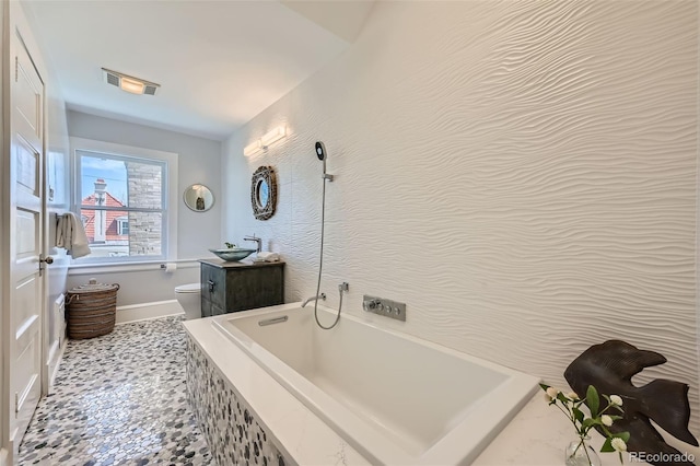 full bath featuring visible vents, vanity, toilet, baseboards, and a bath