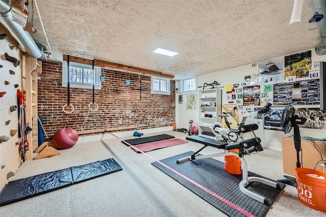exercise area featuring carpet flooring, a textured ceiling, and brick wall