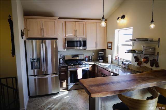 kitchen with light brown cabinets, appliances with stainless steel finishes, a peninsula, vaulted ceiling, and hanging light fixtures