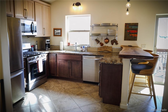 kitchen with dark stone countertops, a kitchen breakfast bar, appliances with stainless steel finishes, a peninsula, and a sink