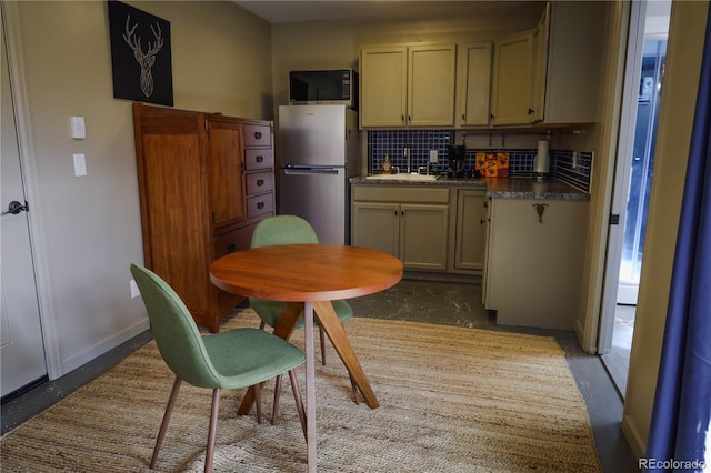 kitchen with baseboards, freestanding refrigerator, a sink, dark countertops, and tasteful backsplash