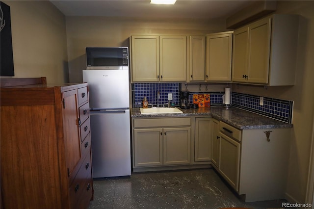 kitchen with a sink, decorative backsplash, dark countertops, and freestanding refrigerator