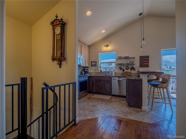 kitchen featuring a peninsula, light wood-style flooring, a kitchen bar, appliances with stainless steel finishes, and a sink
