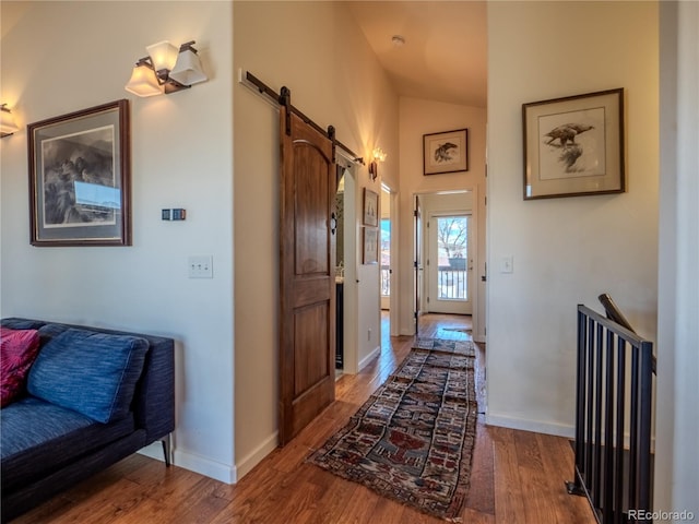 hallway featuring high vaulted ceiling, a barn door, baseboards, and wood finished floors