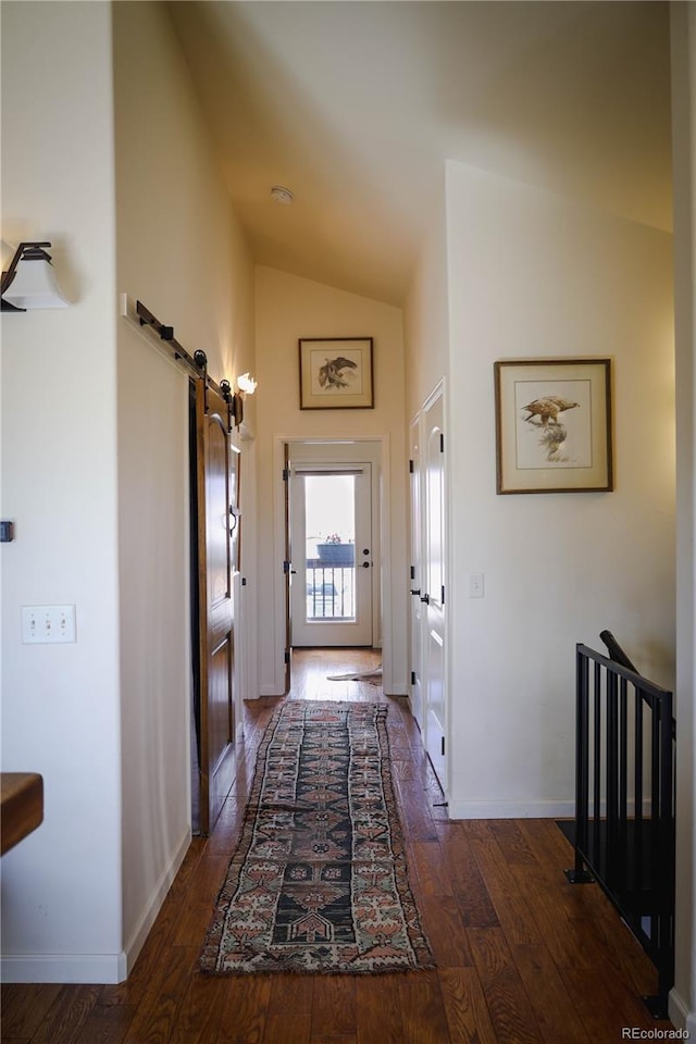 corridor featuring dark wood-style flooring, baseboards, a barn door, and lofted ceiling