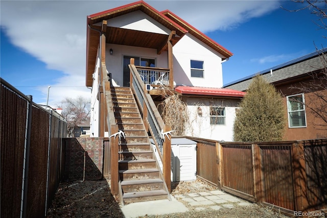 rear view of property with a shed, a fenced backyard, stairway, stucco siding, and an outbuilding