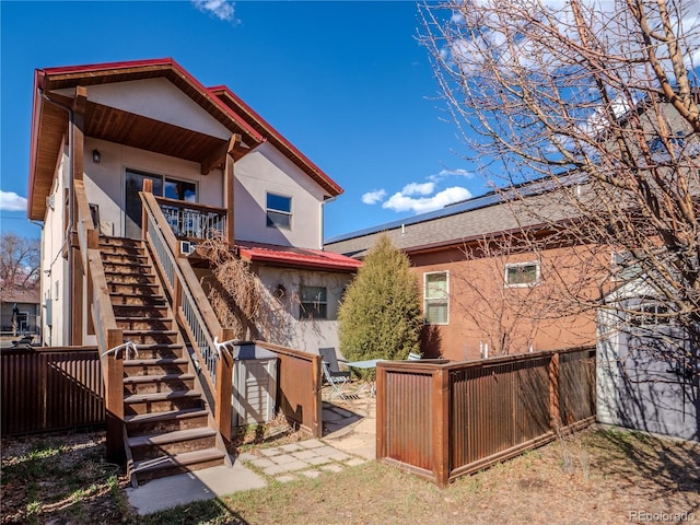 back of house featuring stairs, stucco siding, and fence