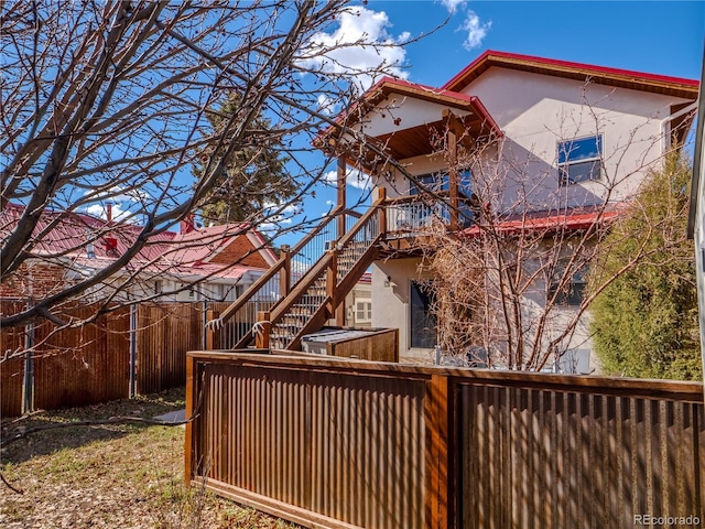 rear view of house featuring a wooden deck, stucco siding, fence, and stairway