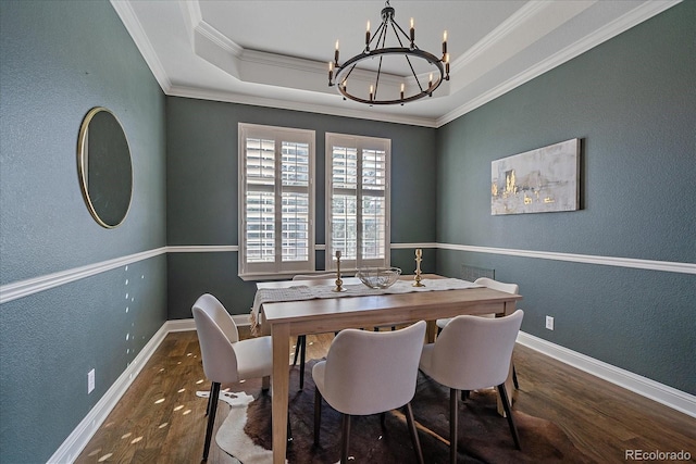 dining area featuring baseboards, ornamental molding, wood finished floors, a notable chandelier, and a raised ceiling