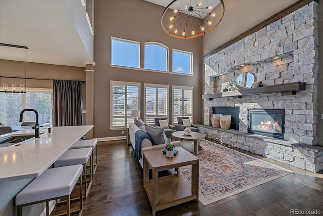 living room with dark wood-type flooring, baseboards, a stone fireplace, a high ceiling, and an inviting chandelier