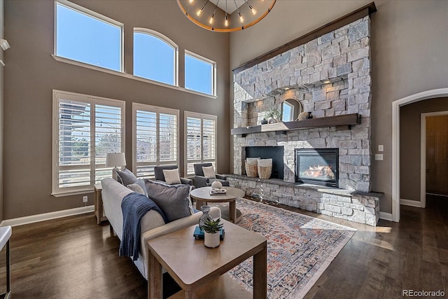 living area with a stone fireplace, a high ceiling, wood finished floors, and baseboards