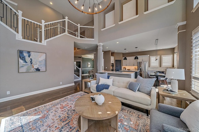 living area featuring baseboards, decorative columns, stairs, dark wood-type flooring, and a notable chandelier