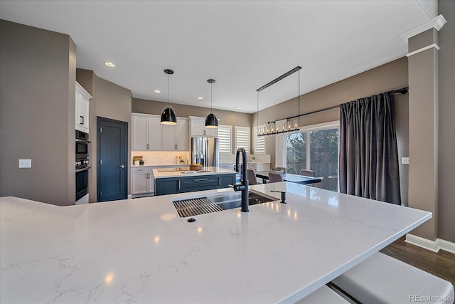 kitchen featuring a sink, decorative light fixtures, a kitchen island, white cabinetry, and appliances with stainless steel finishes