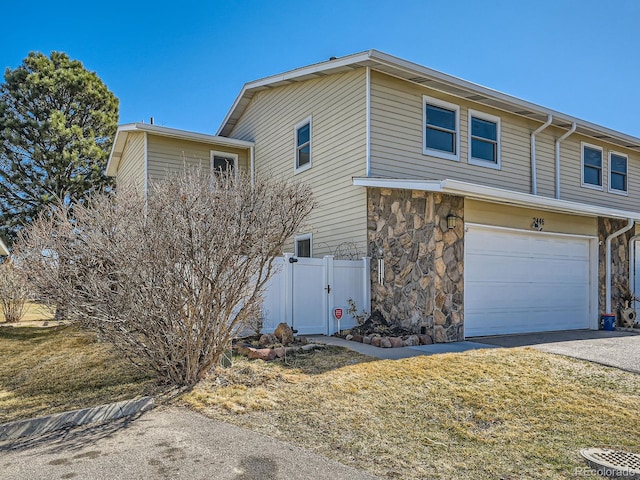 view of side of home with an attached garage, fence, stone siding, driveway, and a gate