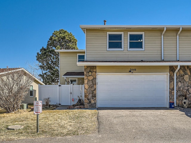 view of front of house with aphalt driveway, an attached garage, fence, stone siding, and a gate