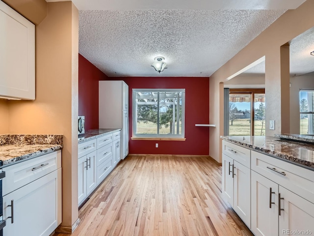 kitchen with light wood-type flooring, stone counters, white cabinetry, and a textured ceiling